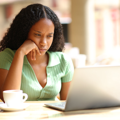 Confused black woman checking laptop in cafe.